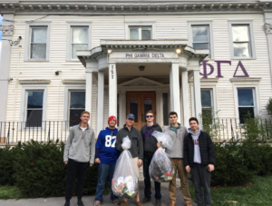 6 men in front of fraternity house with bags of trash