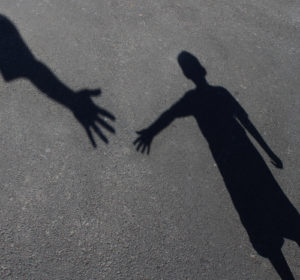 two shadow figures on pavement extend hands toward each other