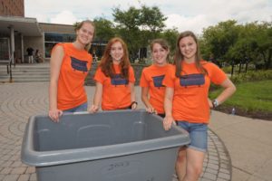 4 college women dressed in orange Goon Squad tshirts standing around a large plastic bin in the Sadler courtyard area