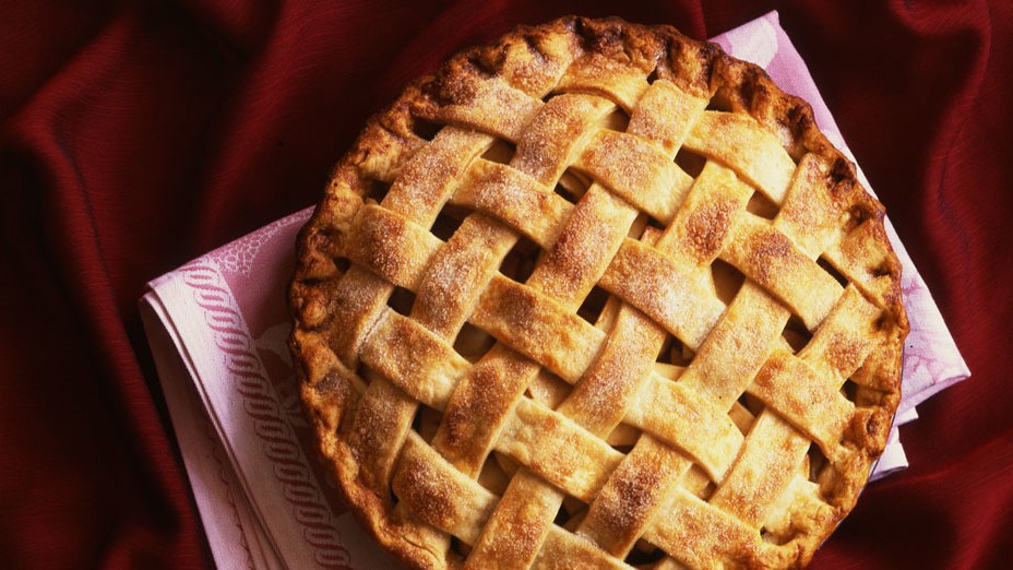 overhead shot of a fresh baked apple pie with a lattice crust on a maroon table cloth