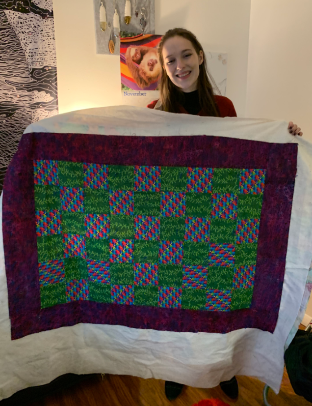 Jenna Merry stands behind geometrical quilt she made